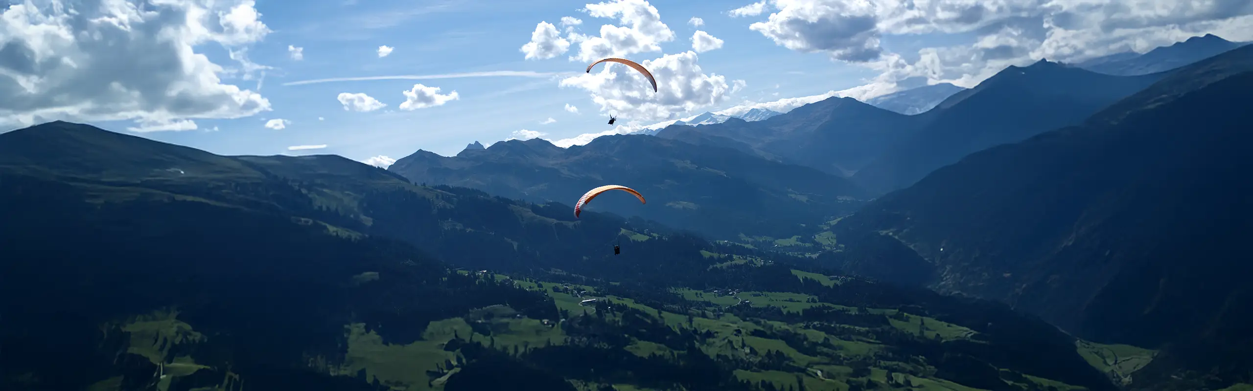 Zwei Gleitschirme über dem grünen Tal von Westendorf in den Kitzbüheler Alpen